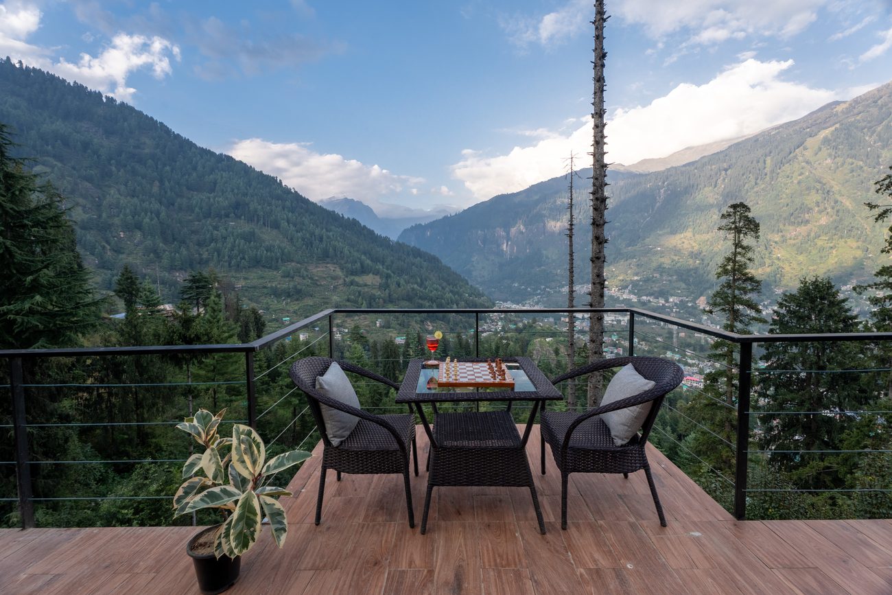 A deck table set with a chess board and armchairs above the valley.