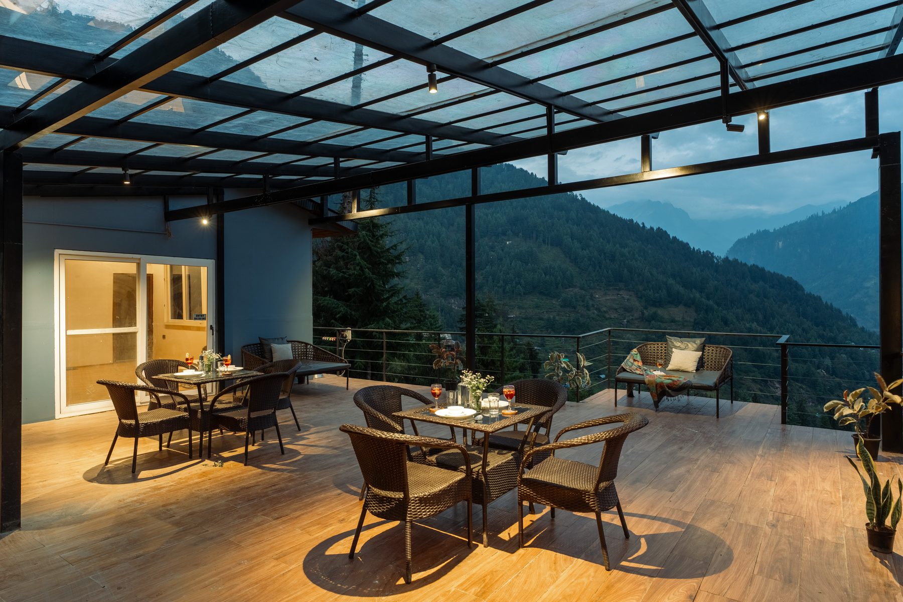The café deck at dusk, warmly lit, tables laid for the evening.