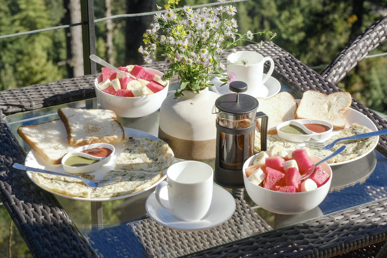 A breakfast table on the deck: fruit bowls, toast, eggs, a cafetiere and wildflowers.