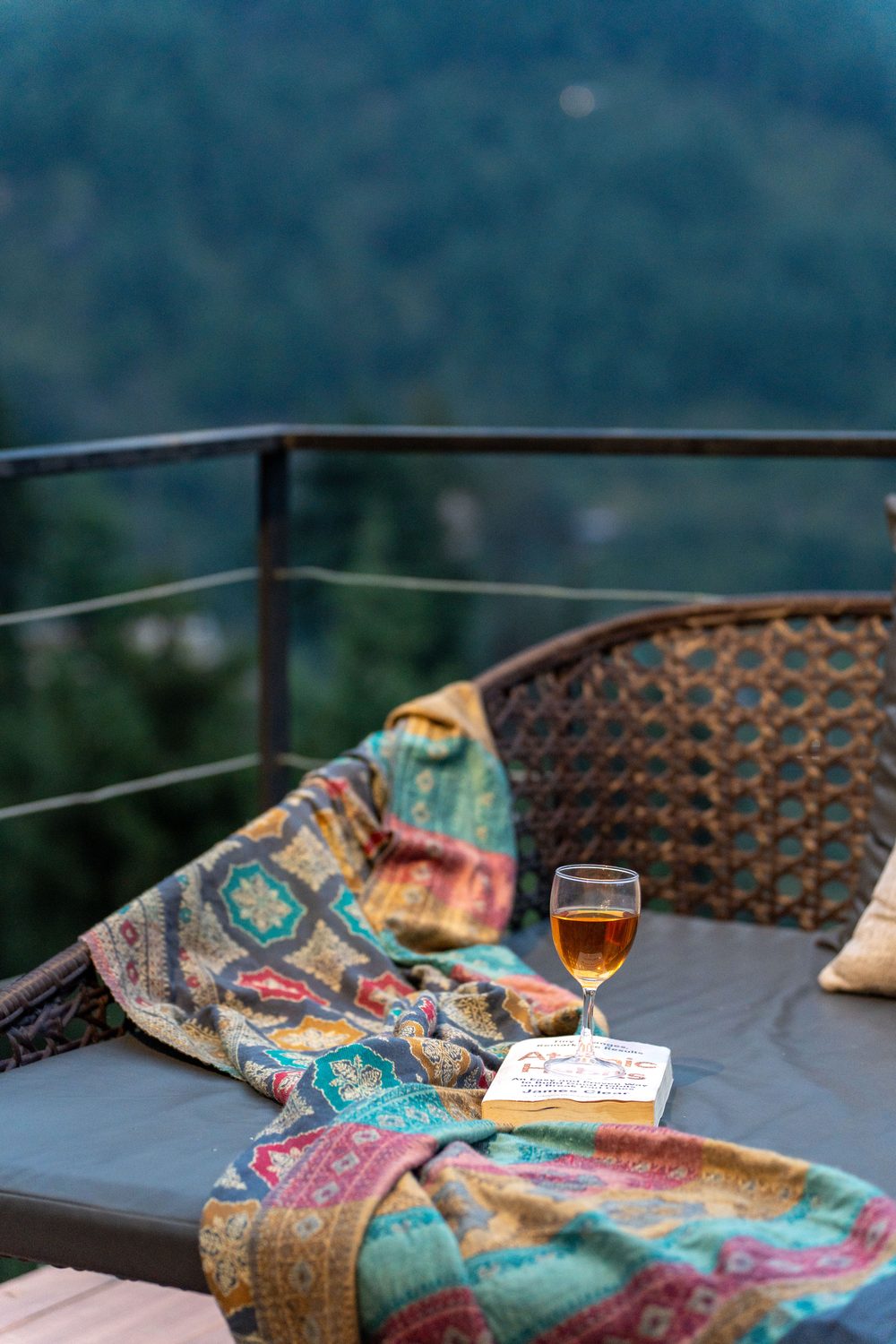 A lounge seat on the deck with a patterned throw and a drink.