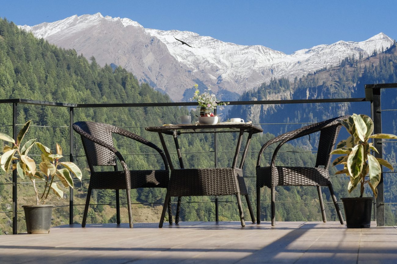 An empty deck table and chairs facing snow peaks.