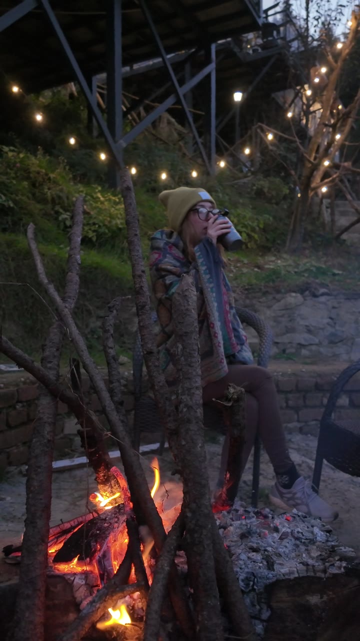 A guest by a crackling fire under string lights.