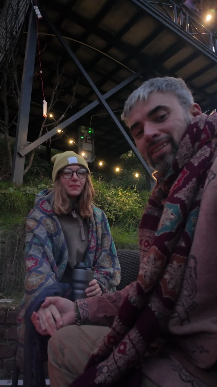 Two guests talking over hot drinks beneath string lights.