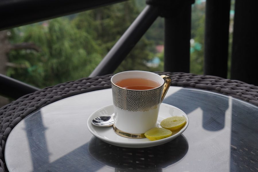 A cup of tea with lemon on a glass table, the railing behind.