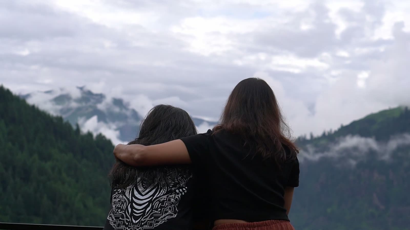 Two women with their arms around each other watching cloud drift across the mountains.